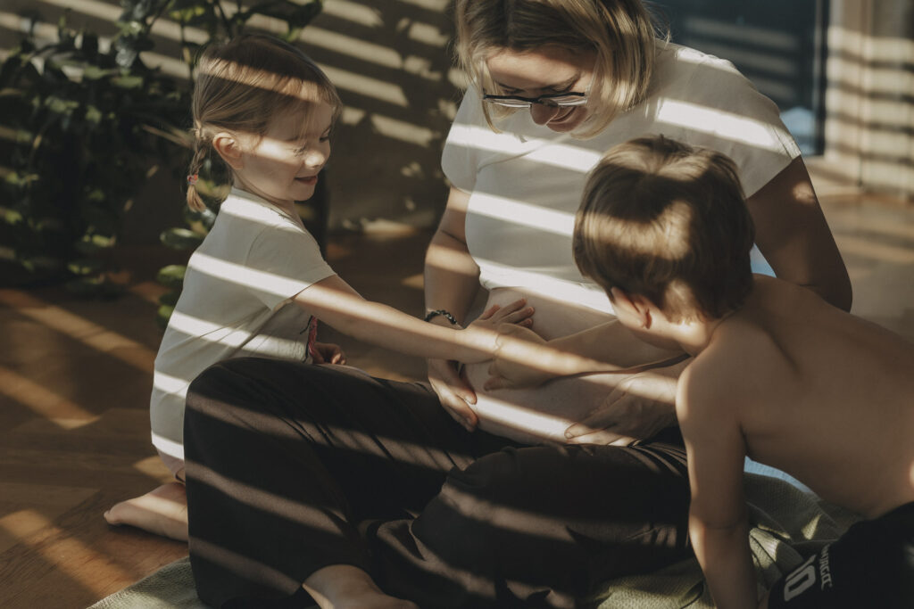 Mama mit zwei Kindern, die ihren Babybauch streicheln - in warmen Sonnenlicht.