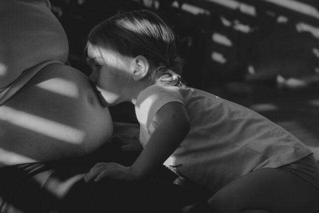 Mädchen küsst Babybauch. Bind in schwarz-weiß.