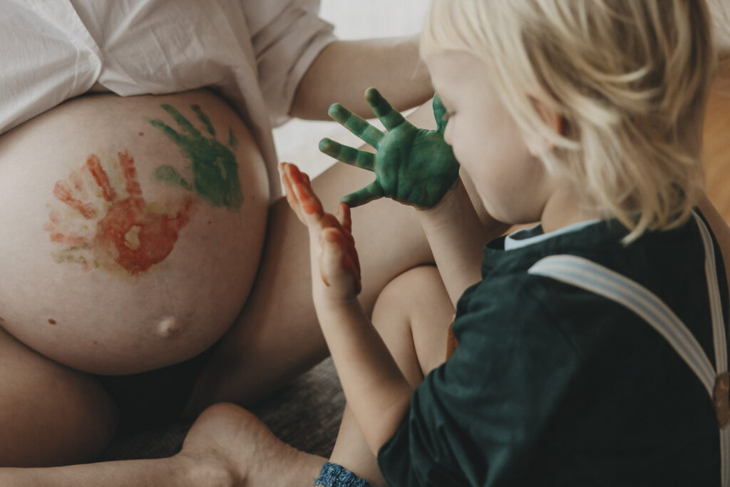 Kinder hat Händeabdruck auf den Schwangerschaftsbauch seiner Mutter gemacht. Er staunt wegen der roten und grünen Finger.
