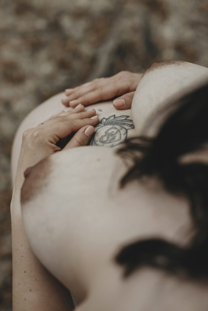 Eine nackte Frau mit Babybauch, von oben fotografiert. Man erkennt ihre Brüste, der Fokus liegt auf den Händen, die auf dem Bauch ruhen.