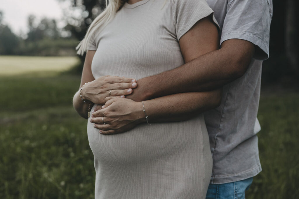 Mann und Frau halten gemeinsam den Babybauch und berühren sich mit den Händen dabei. Es sind keine Gesichter erkennbar.