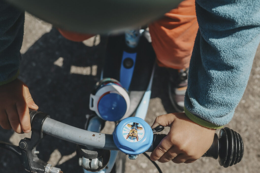 Junge auf einem Rad. Man sieht nur die Hände auf den Griffen und er läutet mit dem Daumen die Glocke.
