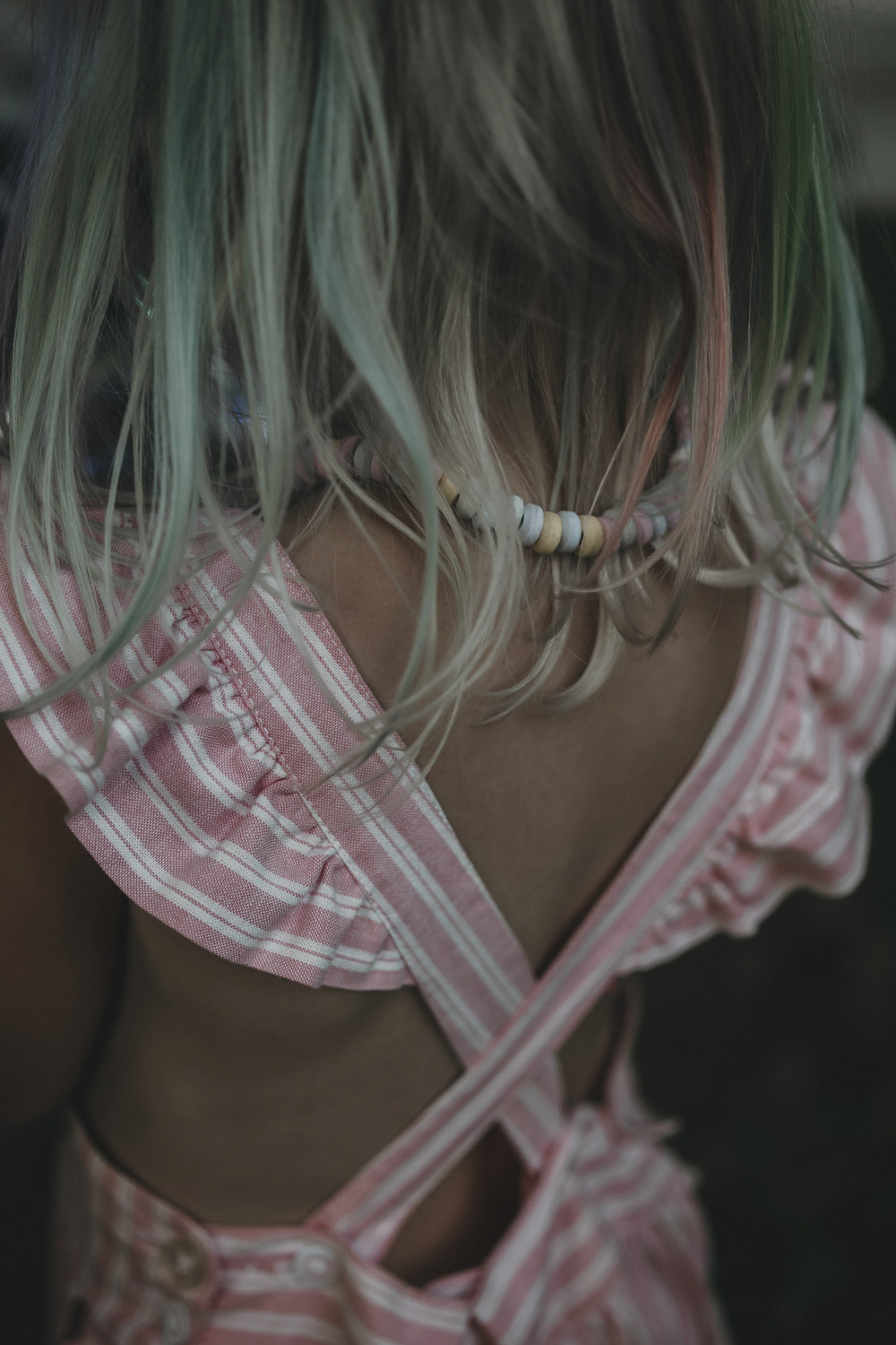 Rücken eines Mädchens in einem rosa Kleid. Ihre Haare sind bunt gefärbt. Am Hals trägt sie eine bunte Kette aus Süßigkeiten.