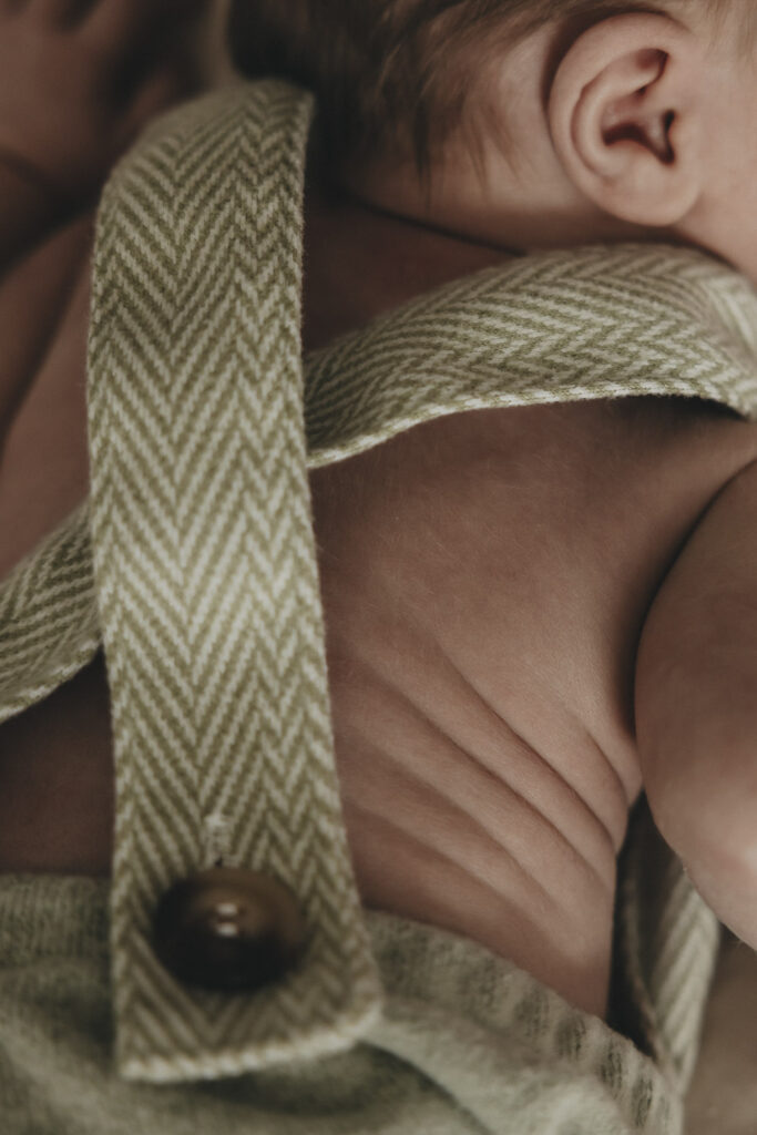 Neugeborenes in einer Hose. Das Kind liegt am Bauch und man erkennt die süßen Speckfältchens des Babys