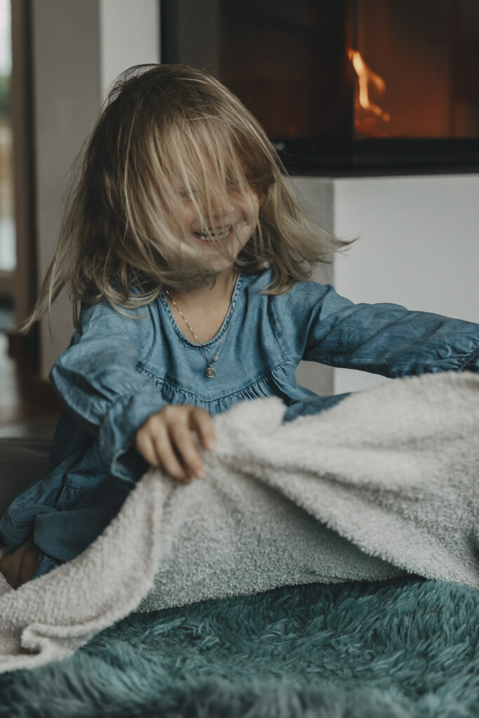 Mädchen, das wild mit einer Decke spielt. Die Haare fallen ihr ins Gesicht.