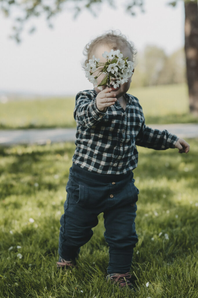 Junge in einem karrierte Hemd, er hält einen Strauß Blumen vor sein Gesicht.