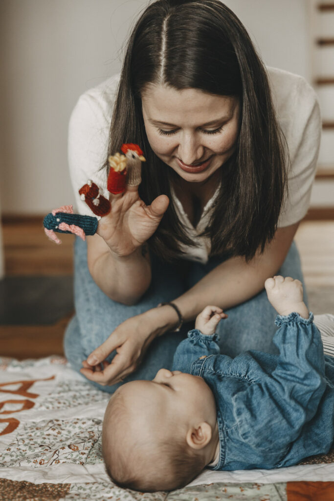 Mama, die verschiedene Puppen auf den einzelnen Fingern hat und ein Baby, das sie aufgeregt beobachtet.