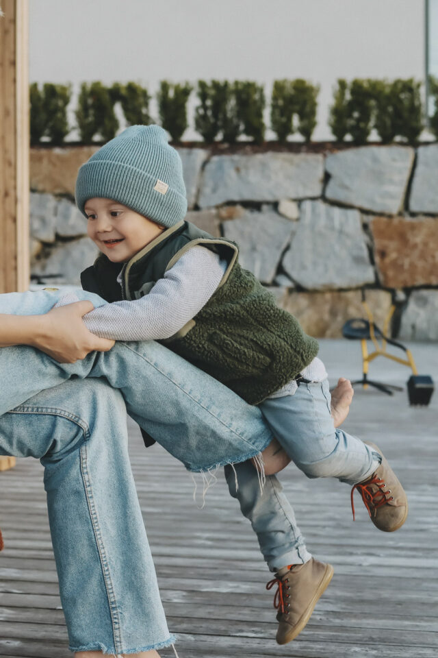 Zweijähriger schaukelt auf dem Fuß seiner Mama.