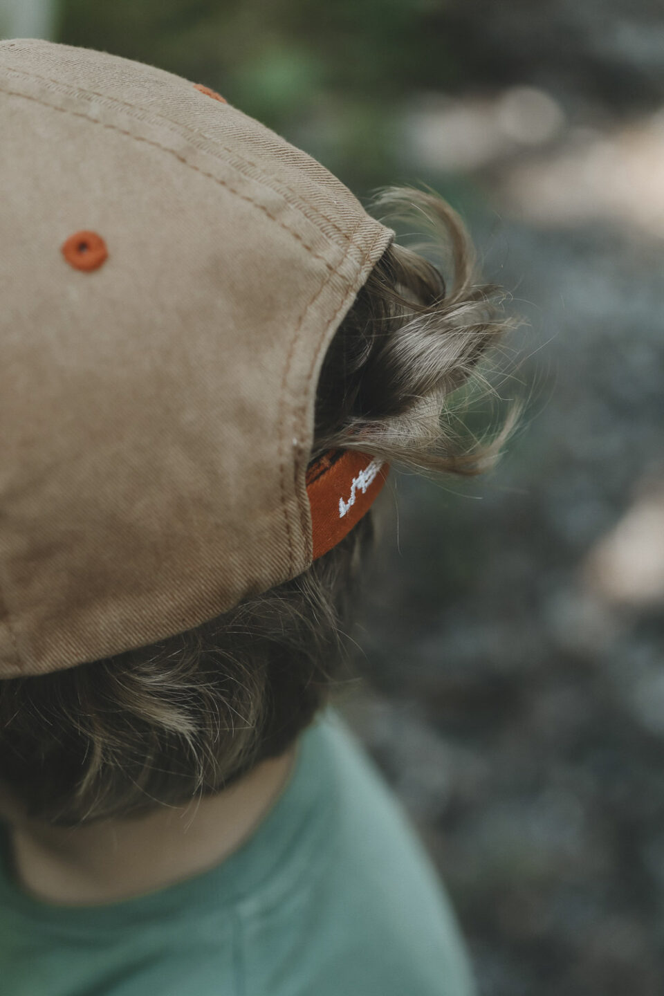 Junge, von hinten. Er trägt eine Kappe und die Haare kräuseln sich hervor.