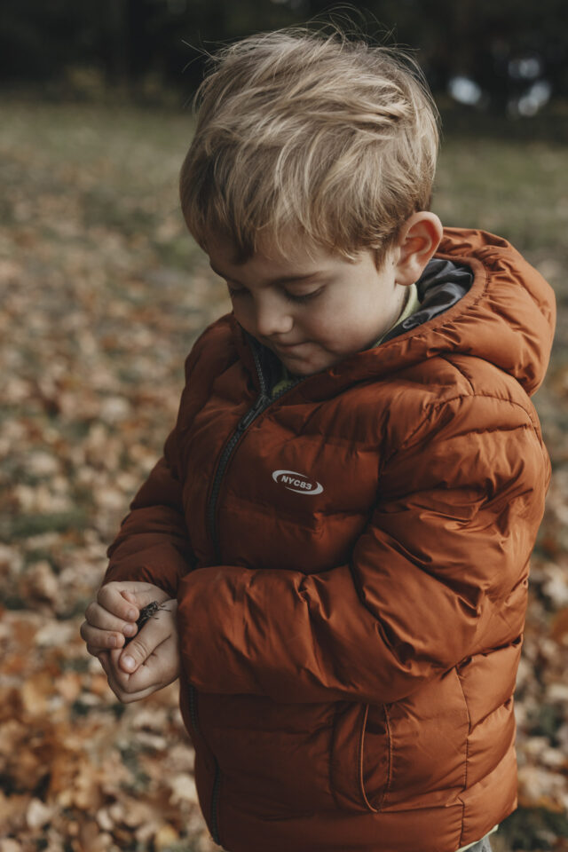 Kind in einer dicken Jacke, das gerade einen Käfer gefangen hat und vorsichtig bestaunt.