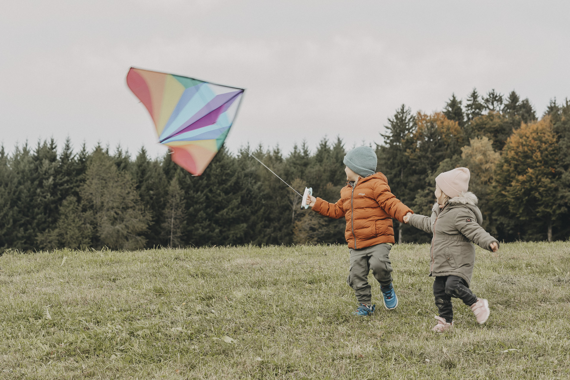 Zwei Kinder Hände haltend beim Drachensteigen.