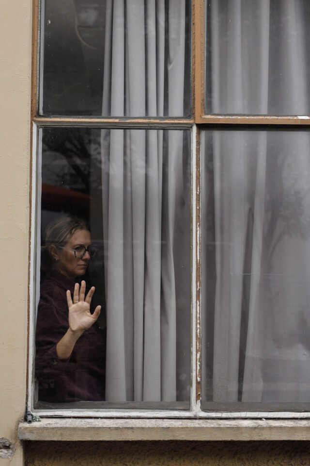 Frau in einer großen Fensterscheibe. Eine Hand berührt das Glas. Der Blick ist nachdenklich.