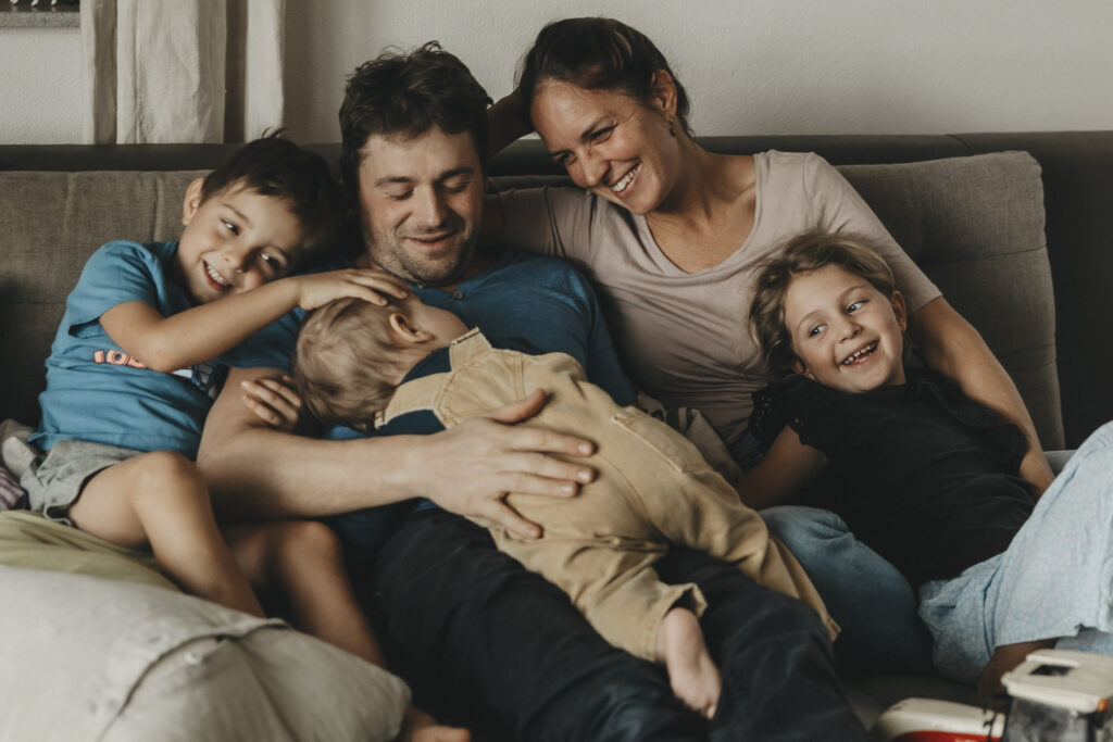 Familie auf einer Couch. Sie betrachten dabei das jüngste Kind und freuen sich.