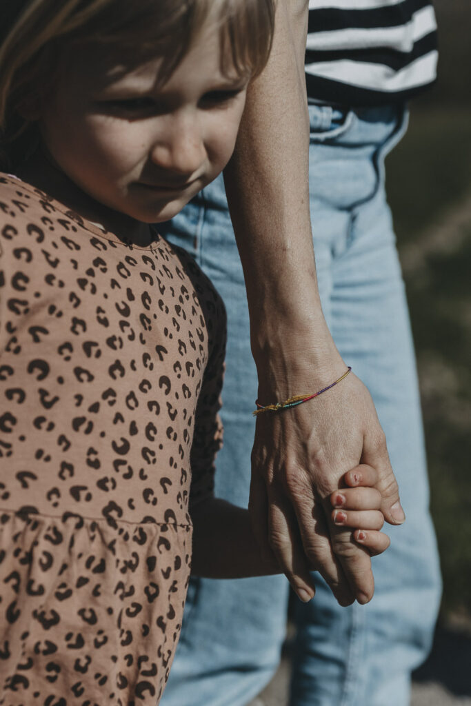 Kind, das die Hand ihrer Mutter hält, während sie spazieren gehen. Im Fokus sind die beiden Hände