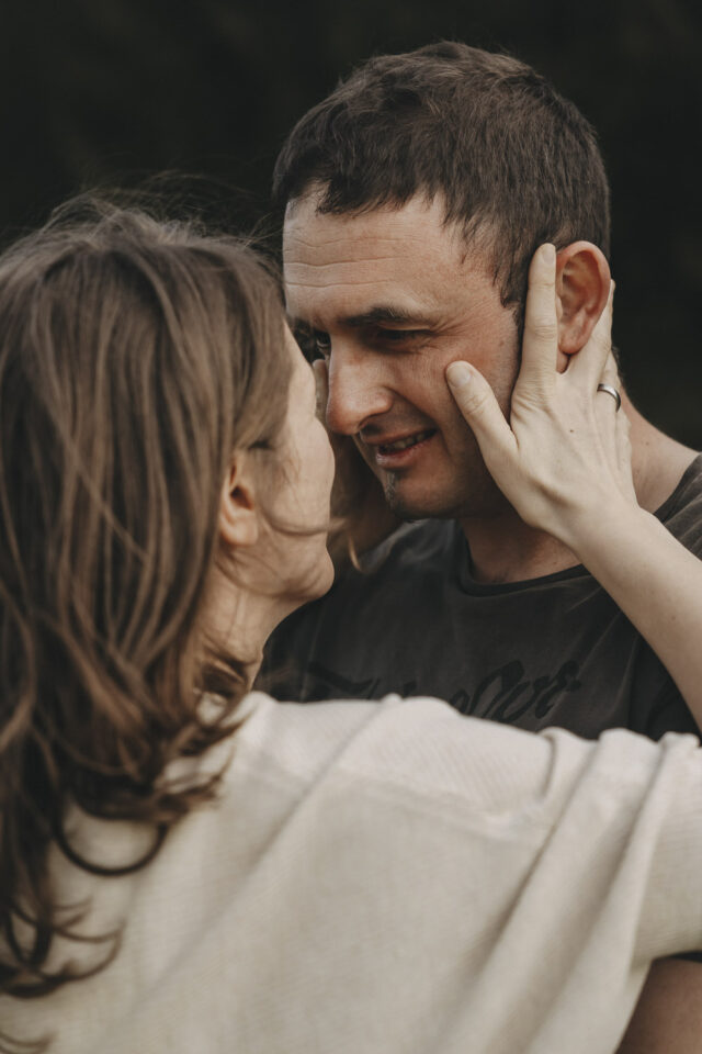 Frau, die ihrem Mann gegenüber steht und mit beiden Händen am Gesicht festhält. Der Moment vor einem Kuss.