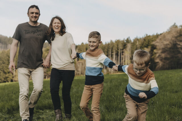 Familie mit vier Personen, alle halten sich an den Händen und laufen in einer Schlange.