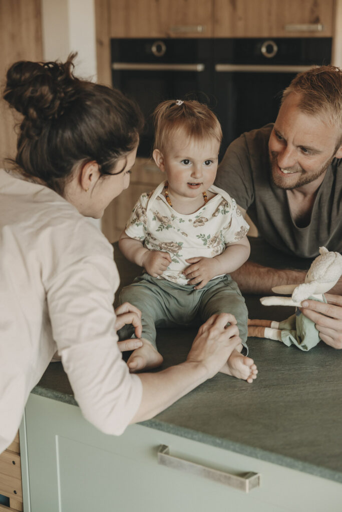 Kind sitzt auf der Kücheninsel, während es mit Mama und Papa spielt.