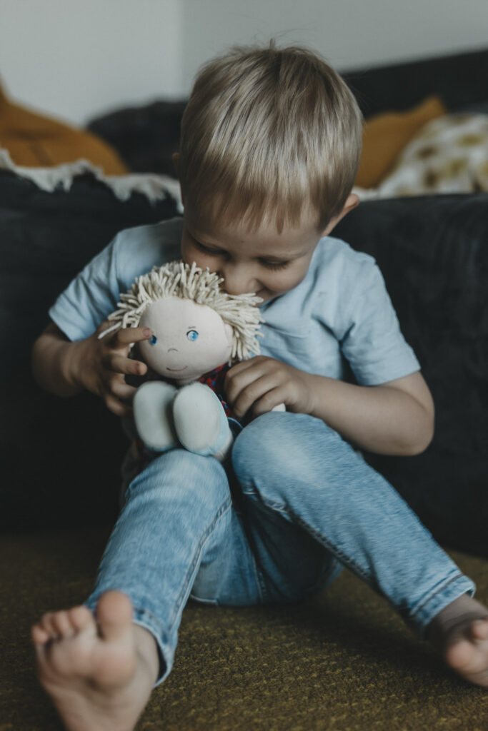 Junge, der mit seiner Puppe spielt. Seine Füße sind barfuß.