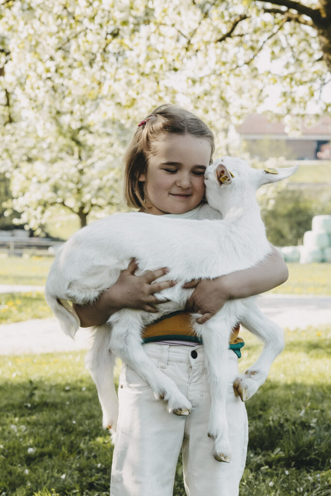Mädchen, dass eine kleine Ziege hochhebt und es liebevoll an sich drückt.