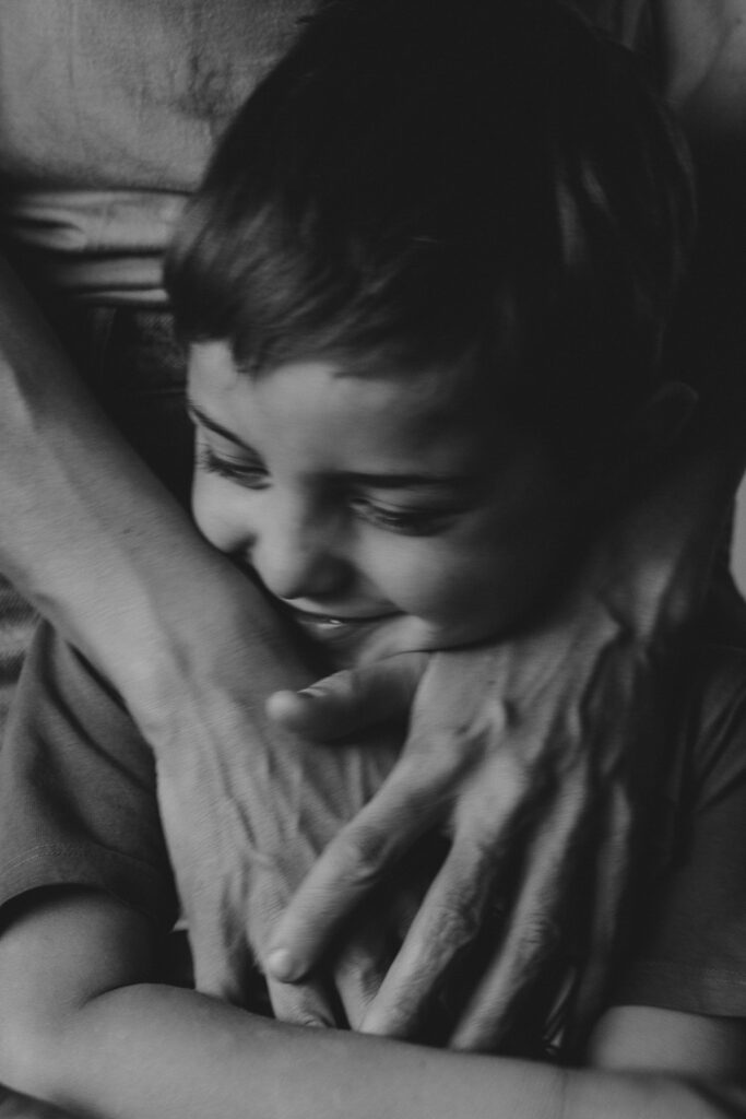 Mutterhände die ihren Jungen ganz fest an sich drückt. Der Junge lächelt und genießt. Schwarz-Weiß-Bild.