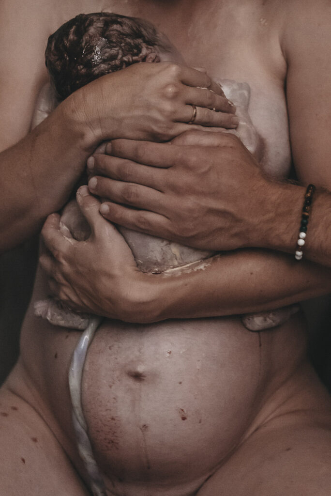 Neugeborenes Baby auf der Brust der Mutter, getragen von den Händen der Eltern.