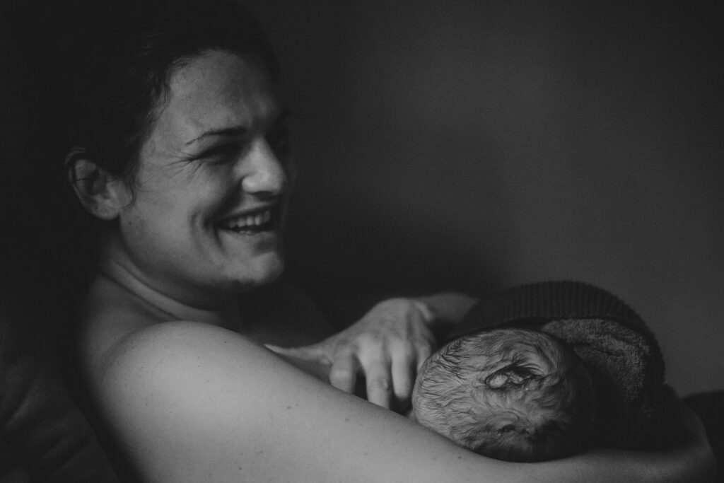 Schwarz-Weiß-Bild. Lachende, erleichterte Frau stillt ihren Säugling das allererste Mal.