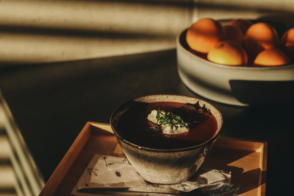 Wärmende Rote-Rüben-Suppe, wunderbar angerichtet. Fotografiert in warmen Sonnenlicht. Im Hintergrund eine Schüssel voll Orangen.