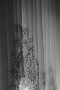 Schwarz-Weiß-Bild. Alte Vorhanggardinen mit Spitze, in Falten, sodass ein Licht- und Schattenspiel entsteht.