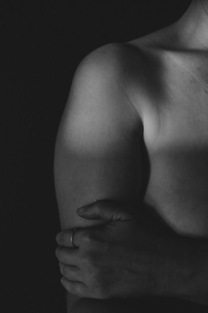 Schwarz-Weiß-Bild. Schulter und Hand einer nackten Frau. Festhaltend.