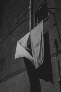 Schwarz-Weiß-Bild. Zwei weiße Handtücher auf einer Wäscheschnur an einem Hochhaus, wehend im Wind.