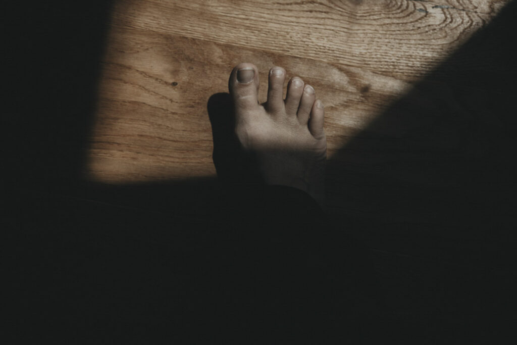 Fuß, der in ein Lichtfenster eintreten möchte, allerdings vorher stoppt und zögert.