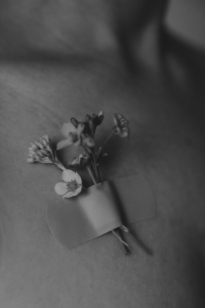 Schwarz-Weiß-Bild. Blümchen die mit einem Pflaster auf dem Dekolleté einer Frau festgeklebt sind.