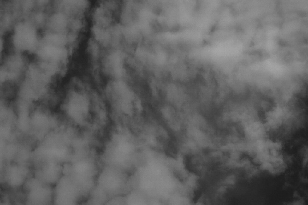 Schwarz-Weiß-Bild. Helle, luftige Wolken vor einem dunklen Himmel.