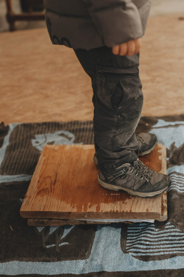 Kinderfüße die auf zwei Holzplatten stehen, um das geschöpfte Papier zu pressen.