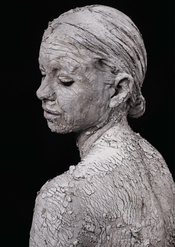 Wunderschöne Frau dargestellt mit weißer, bröckelnder Heilerde. Wirkt wie eine Fassade.