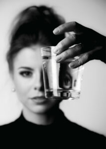 Schwarz-Weiß-Bild. Frauenkopf der zur einen Hälfte hinter ein Glas versteckt ist, sodass sich eine verzehrte Spiegelung ergibt.