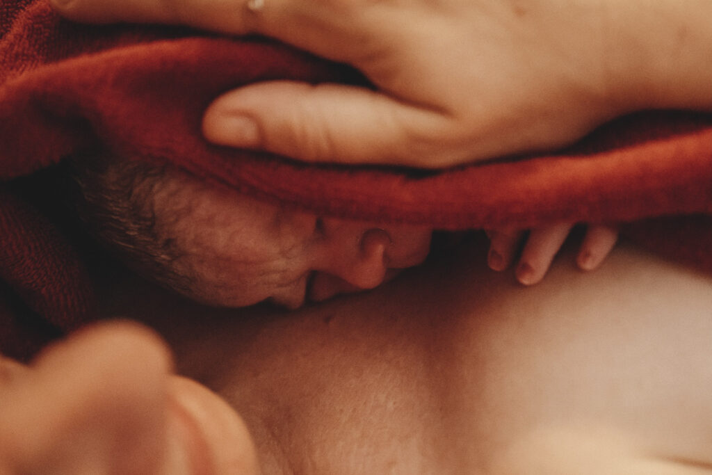Neugeborenes Baby auf der Brust der Mutter, eingewickelt im roten Handtuch.