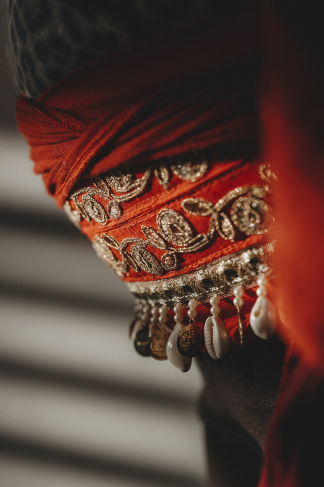 Roter Gürtel mit Muscheln, Perlen und Fäden.