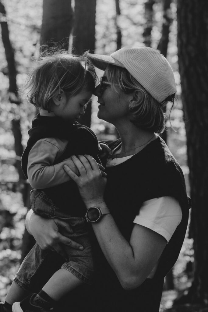 Eine Frau, die ihre Tochter in den Armen trägt und sie auf die Stirn küsst. Schwarz-Weiß-Bild.