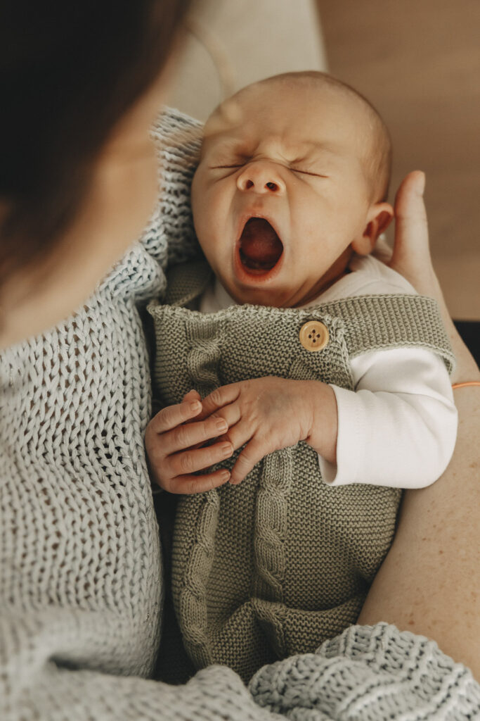 Gähnendes Baby mit offenem Mund in den Armen der Mama.