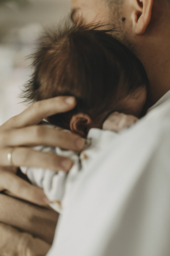 Neugeborenes mit vielen Haaren auf der Brust seines Vaters.