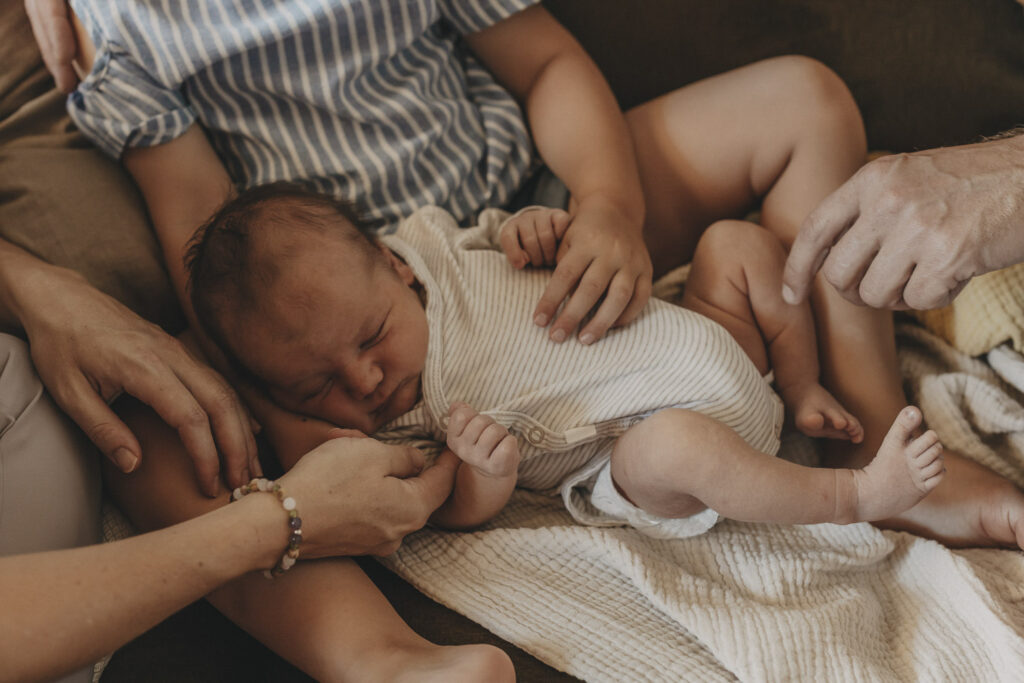 Baby inmitten seiner Familie. Die Hände von Mama, Papa und Schwester streicheln das kleine Kind.