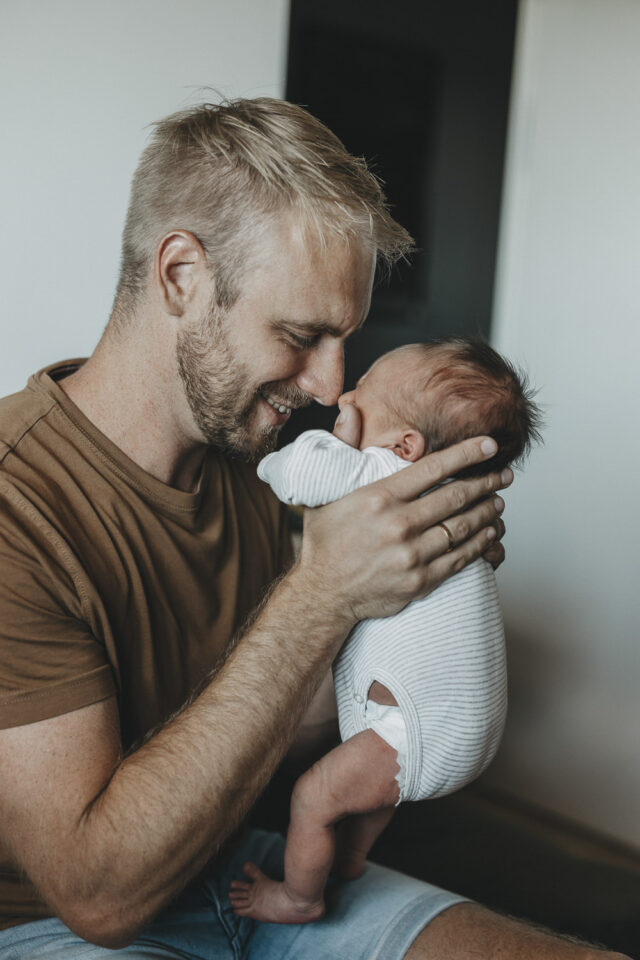 Vater hält sein Neugeborenes. Nase auf Nase betrachtet er das Kind stolz.