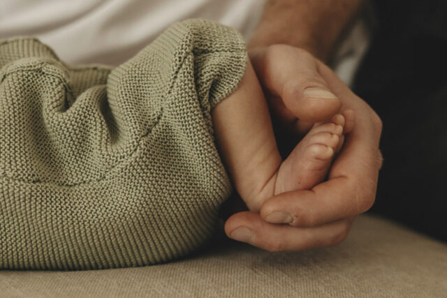 Eine Männerhand hält die Füßchen des Neugeborenen.