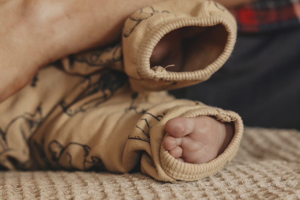 Babyfüßchen in einem Strampler, der noch viel zu groß ist.