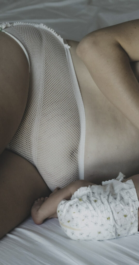 Mutter mit Netzhöschen liegt neben dem Neugeborenen in Windel.