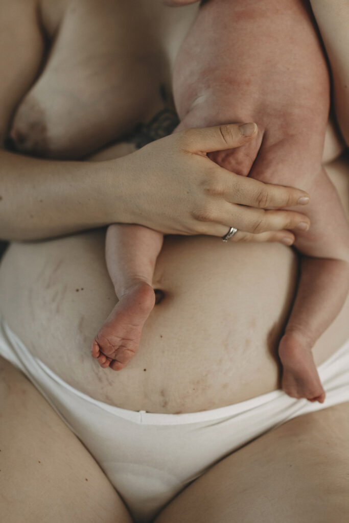 Nacktes Baby liegt auf der Brust der Mutter. Sie trägt nur ein weißes Höschen.