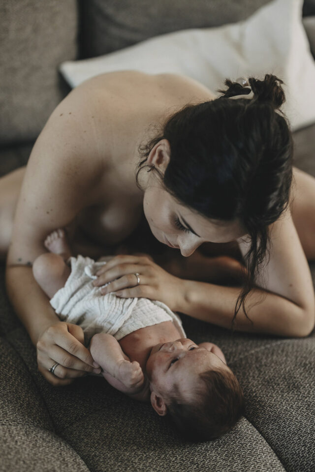 Nackte Frau betrachtet ihr Neugeborenes, das nur in ein Windel gewickelt ist.