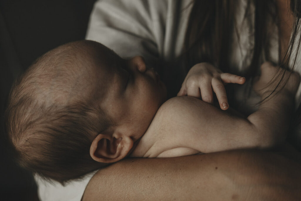 Schlafendes, nacktes Baby in den Händen der Mutter.