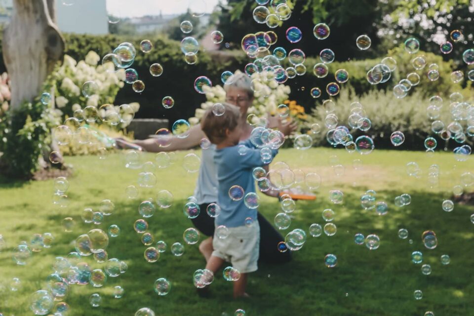 Ein Kind und eine Frau im Garten, rundherum eine Vielzahl von Seifenblasen.